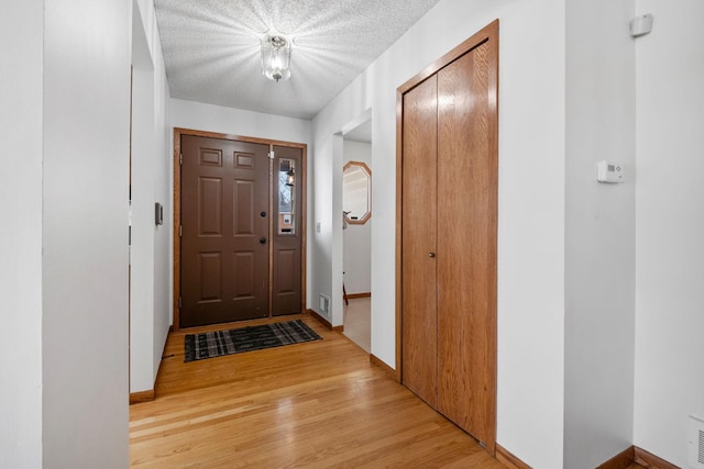 entryway with visible vents, a textured ceiling, light wood-type flooring, and baseboards