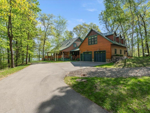 view of front facade with asphalt driveway, an attached garage, stone siding, log veneer siding, and metal roof