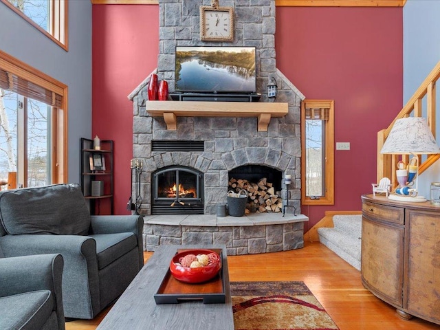 living room with a stone fireplace, wood finished floors, stairs, and a towering ceiling