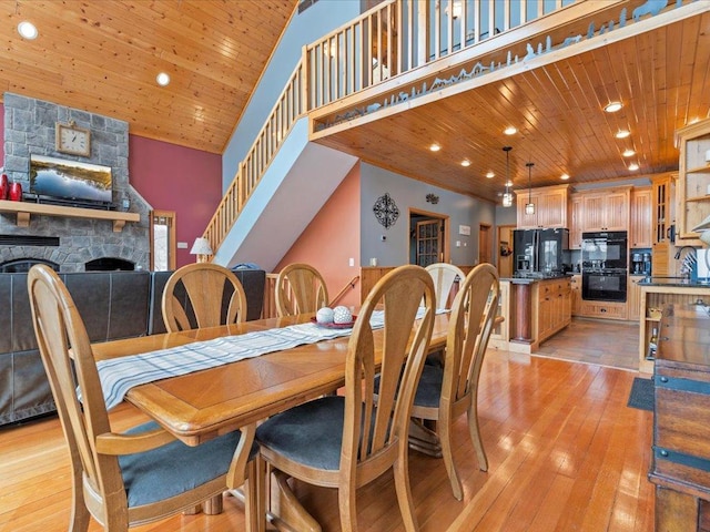dining room featuring a fireplace, light wood-style floors, recessed lighting, wood ceiling, and a high ceiling