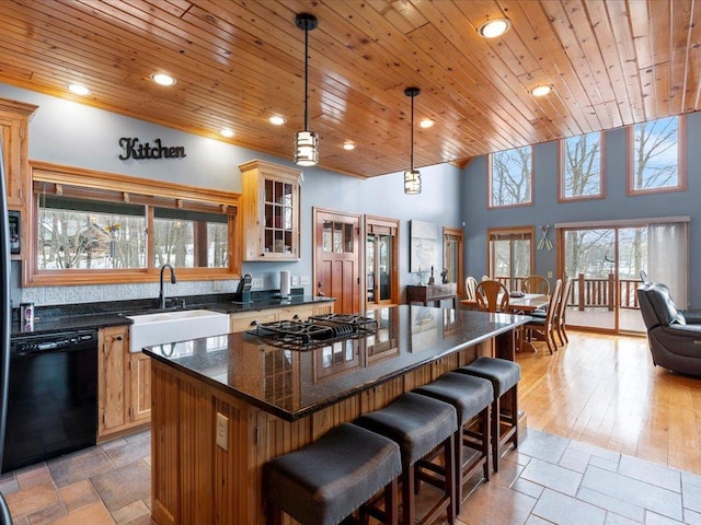 kitchen with black appliances, a sink, wooden ceiling, a kitchen island, and a kitchen bar