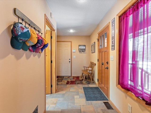corridor featuring healthy amount of natural light, stone finish flooring, and baseboards