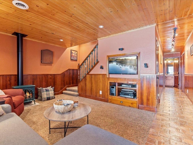 living room featuring wood ceiling, a wainscoted wall, a wood stove, wood walls, and stairway