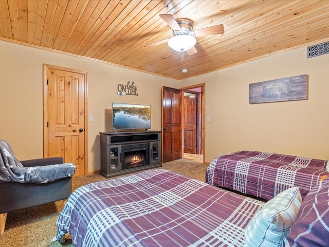 bedroom featuring carpet floors, wooden ceiling, ornamental molding, a ceiling fan, and a warm lit fireplace
