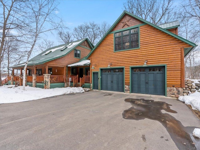 chalet / cabin with driveway, an attached garage, covered porch, log veneer siding, and stone siding