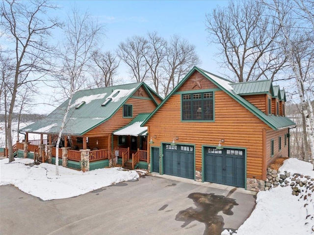 view of front of house with asphalt driveway, a garage, a porch, stone siding, and metal roof