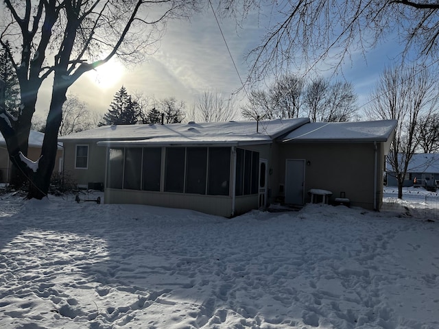 snow covered back of property with a sunroom