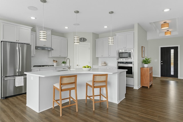 kitchen featuring stainless steel appliances, a sink, dark wood-style flooring, tasteful backsplash, and light countertops
