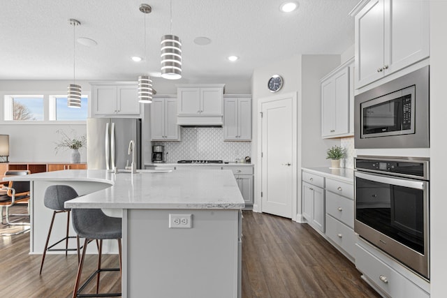 kitchen featuring stainless steel appliances, dark wood finished floors, a kitchen breakfast bar, decorative backsplash, and a textured ceiling