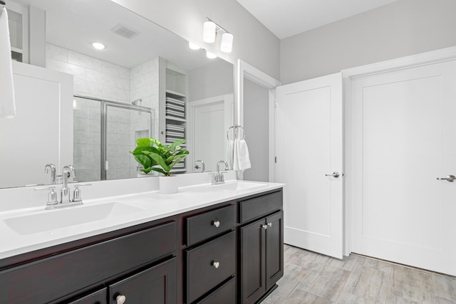 bathroom with a stall shower, double vanity, and wood finished floors