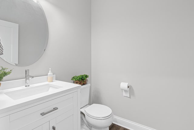 half bathroom with toilet, vanity, wood finished floors, and baseboards