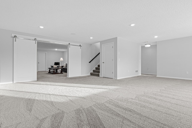 below grade area with a barn door, a textured ceiling, recessed lighting, light colored carpet, and stairway