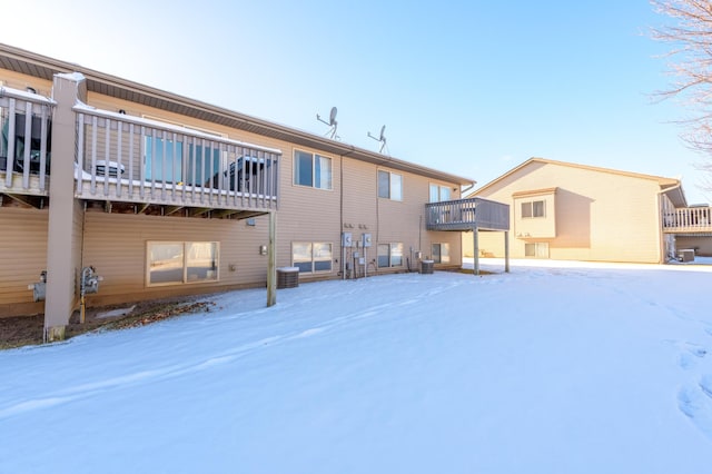 snow covered back of property with a balcony and central AC