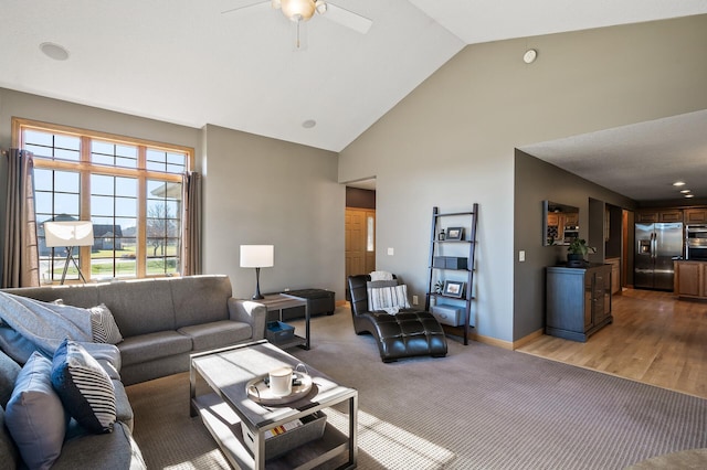 living room with light colored carpet, light wood-style flooring, ceiling fan, high vaulted ceiling, and baseboards