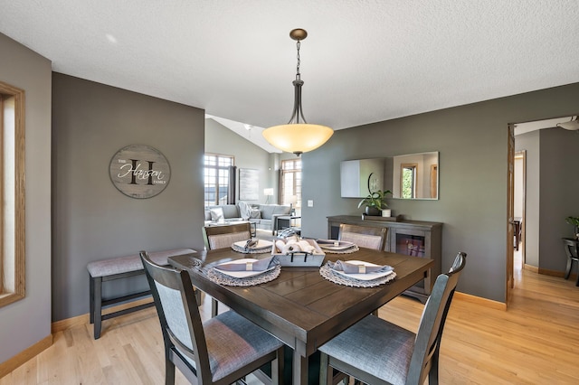 dining area with light wood finished floors, baseboards, vaulted ceiling, and a textured ceiling