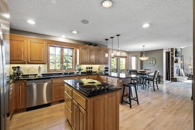 kitchen with appliances with stainless steel finishes, light wood-style floors, brown cabinetry, a sink, and plenty of natural light