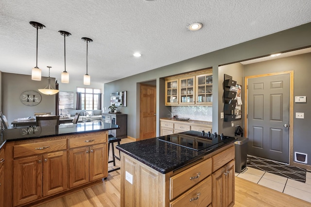 kitchen featuring decorative backsplash, glass insert cabinets, black electric stovetop, light wood-type flooring, and pendant lighting