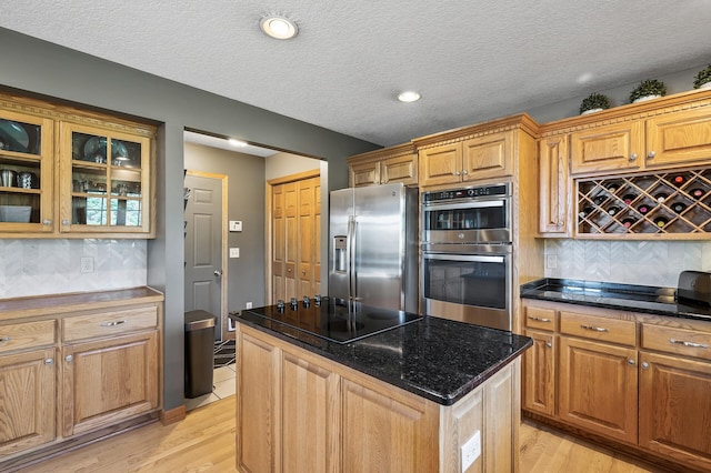 kitchen with light wood-style floors, appliances with stainless steel finishes, a center island, tasteful backsplash, and glass insert cabinets