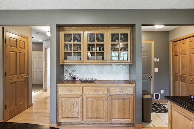 kitchen with glass insert cabinets, backsplash, baseboards, and a textured ceiling