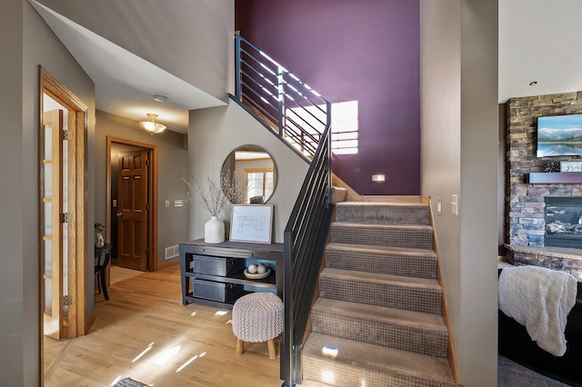 stairway featuring a fireplace, visible vents, a high ceiling, wood finished floors, and baseboards