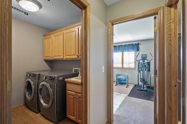 laundry room featuring cabinet space, baseboards, washer and clothes dryer, wood finished floors, and a textured ceiling