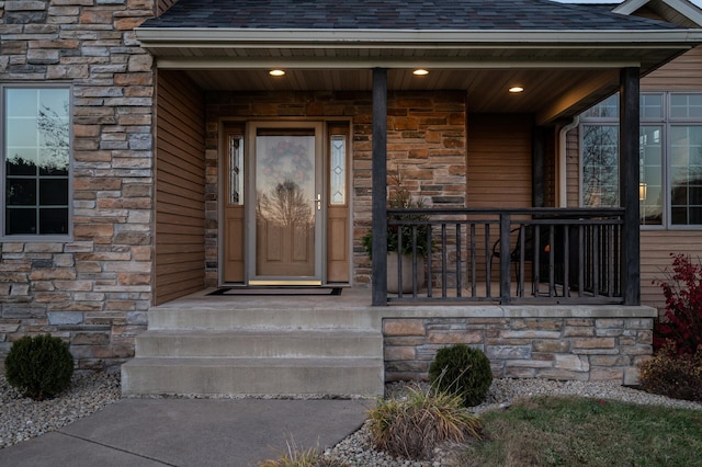 entrance to property with stone siding, a porch, and roof with shingles