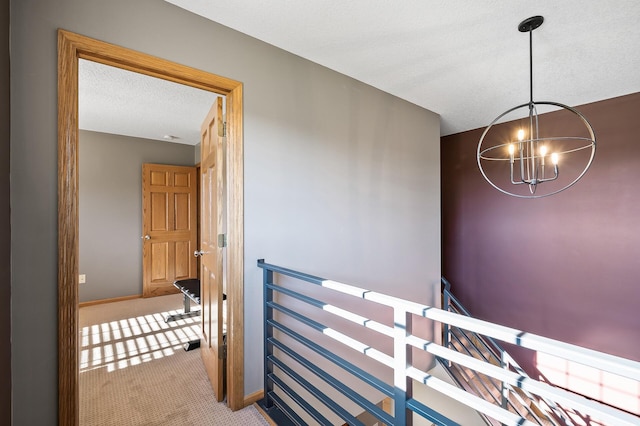 corridor featuring a chandelier, a textured ceiling, carpet flooring, an upstairs landing, and baseboards