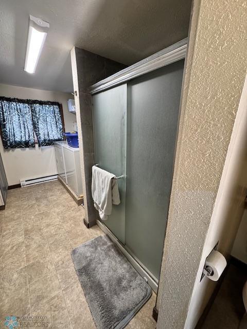 bathroom with washing machine and clothes dryer, a shower with shower door, and a baseboard heating unit