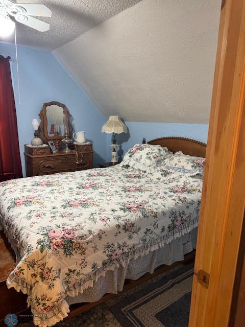 bedroom with ceiling fan, lofted ceiling, and a textured ceiling