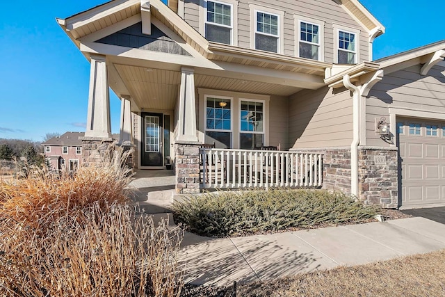 entrance to property with stone siding, covered porch, and an attached garage