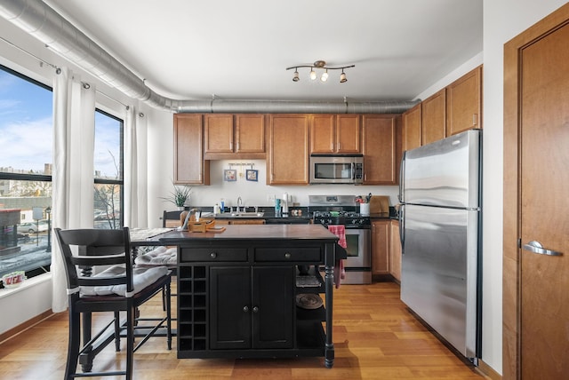 kitchen with stainless steel appliances, dark countertops, brown cabinetry, light wood-style floors, and a sink