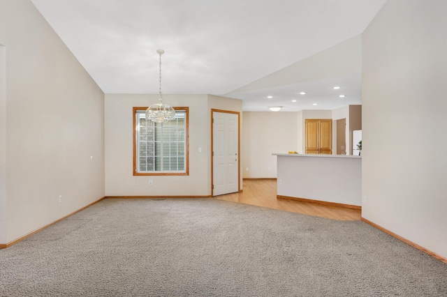 carpeted empty room with lofted ceiling and a chandelier