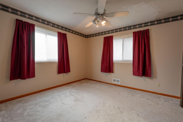 carpeted spare room featuring a wealth of natural light, a textured ceiling, and ceiling fan