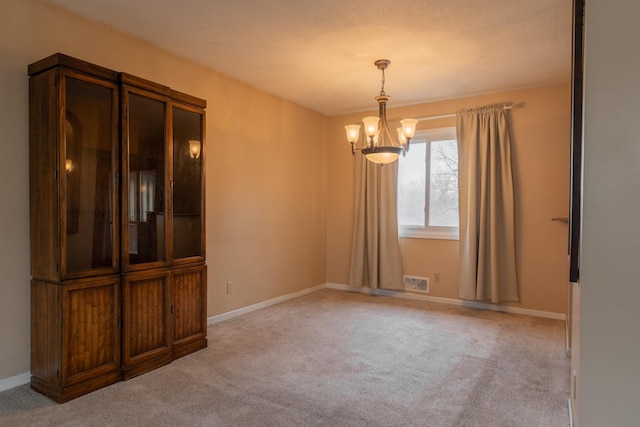 carpeted empty room featuring an inviting chandelier