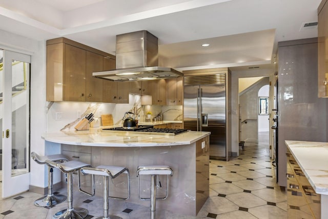 kitchen with stainless steel appliances, a breakfast bar, island range hood, and kitchen peninsula