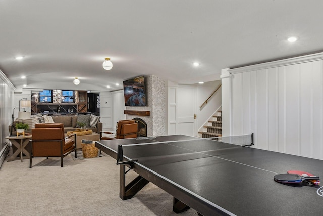 game room with a stone fireplace and light colored carpet