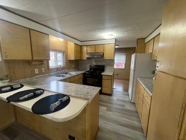 kitchen featuring under cabinet range hood, a peninsula, a sink, black gas stove, and light countertops