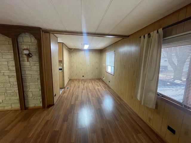 empty room with wooden walls, wood finished floors, and a healthy amount of sunlight