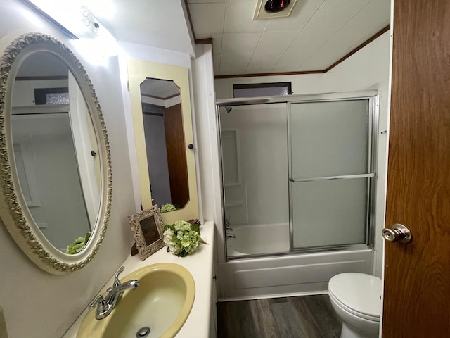 full bathroom featuring toilet, ornamental molding, combined bath / shower with glass door, a sink, and wood finished floors