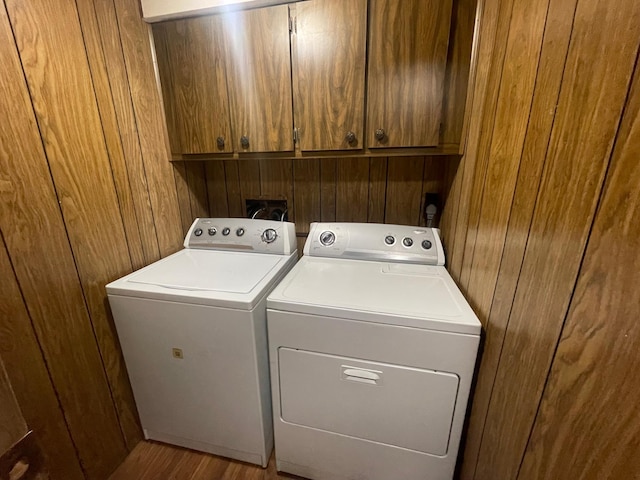 laundry room with cabinet space, wooden walls, and washing machine and clothes dryer