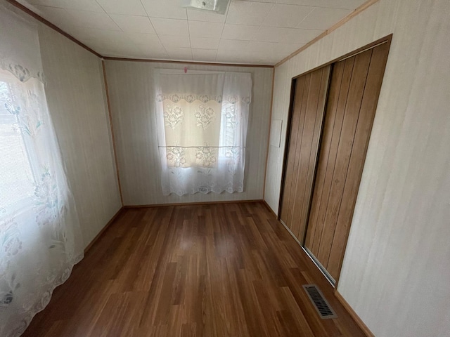 unfurnished bedroom with a closet, visible vents, dark wood-style flooring, and crown molding