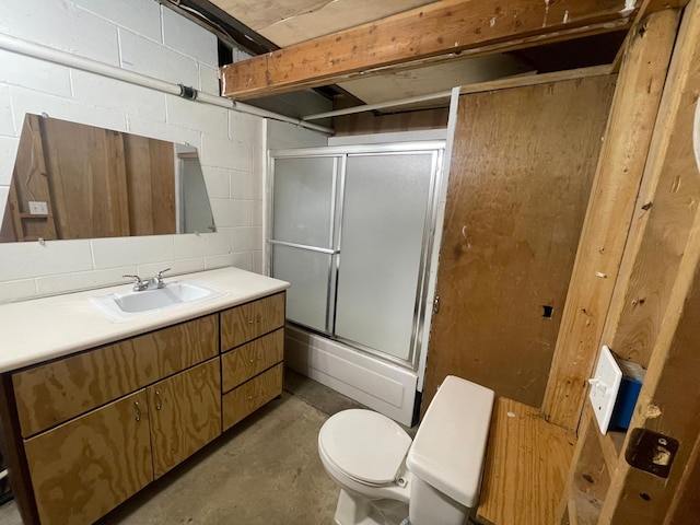 full bath featuring concrete block wall, unfinished concrete flooring, toilet, shower / bath combination with glass door, and vanity