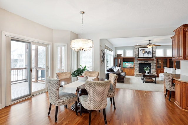 dining room featuring ceiling fan with notable chandelier, a fireplace, and light wood-type flooring