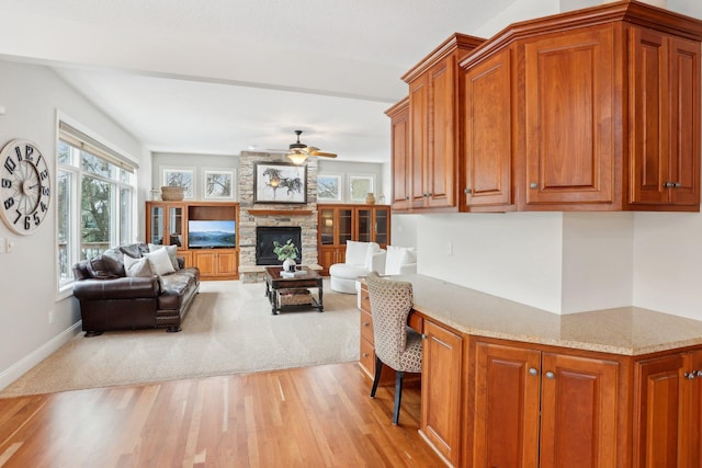 living room with a stone fireplace, light hardwood / wood-style flooring, built in desk, and ceiling fan