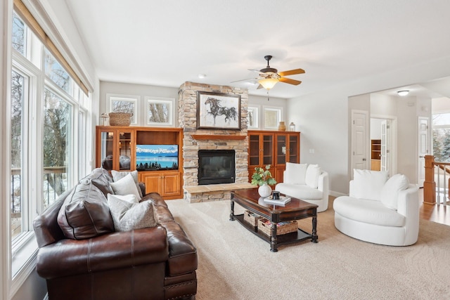 living room with a stone fireplace, a healthy amount of sunlight, and ceiling fan