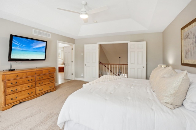 carpeted bedroom with ensuite bath, a raised ceiling, and ceiling fan