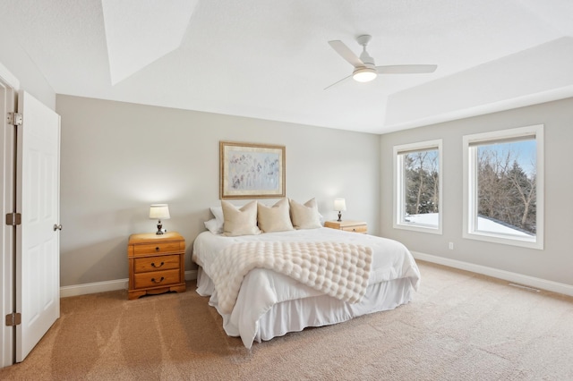 carpeted bedroom with ceiling fan and a raised ceiling