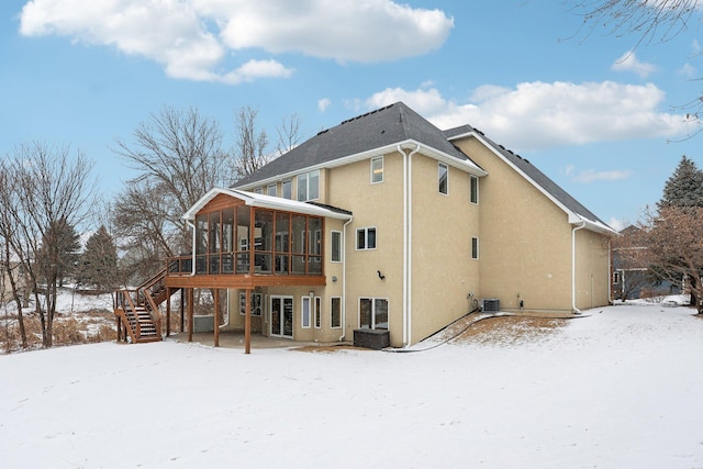 snow covered back of property featuring a sunroom and central air condition unit