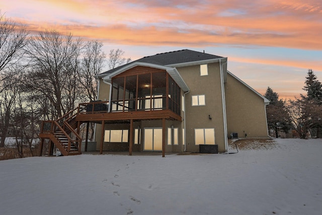 snow covered back of property with a wooden deck and a sunroom