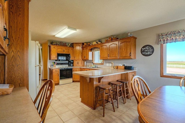 kitchen featuring white electric stove, a healthy amount of sunlight, a breakfast bar, and kitchen peninsula